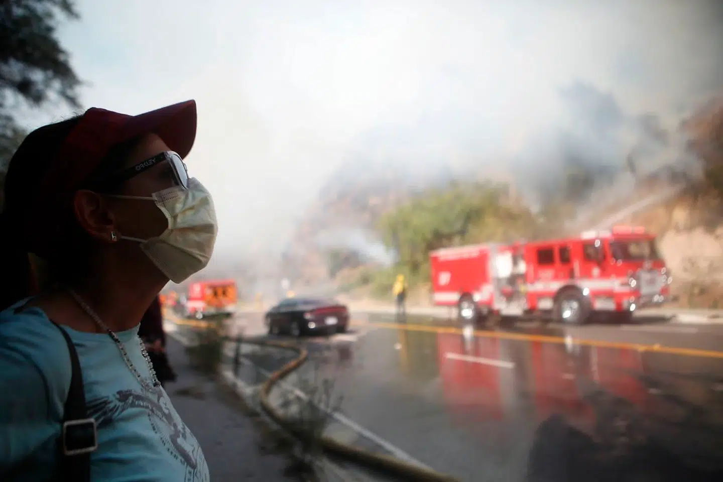 En lokal kvinde bærer en ansigtsmaske, mens hun ser brandfolkene arbejde under branden i Pacific Palisades.