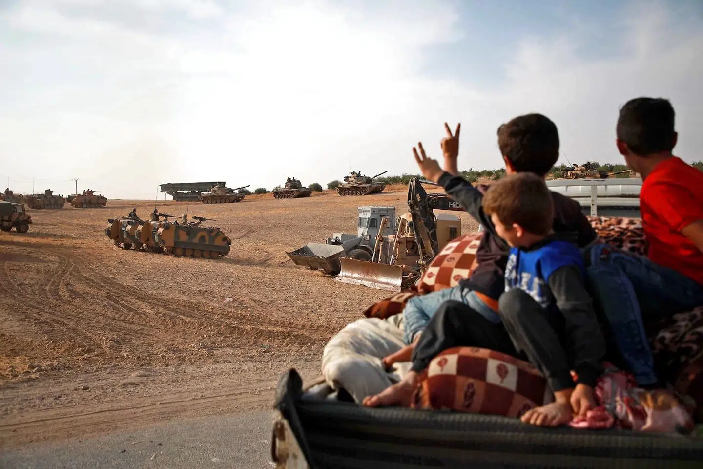TOPSHOT - Syrian Arab civilians flash the victory sign as Turkish armoured personnel carriers and US-made M60 taks gather in the village of Qirata on the outskirts of the northern Syrian city of Manbij near the Turkish border, on October 14, 2019. - Turkey wants to create a roughly 30-kilometre (20-mile) buffer zone along its border to keep Kurdish forces at bay and also to send back some of the 3.6 million Syrian refugees it hosts. (Photo by Aaref WATAD / AFP)