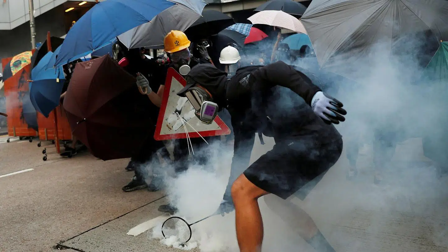 En Hong Kong-demonstrant samler en af politiets røgbomber op med en ketcher.