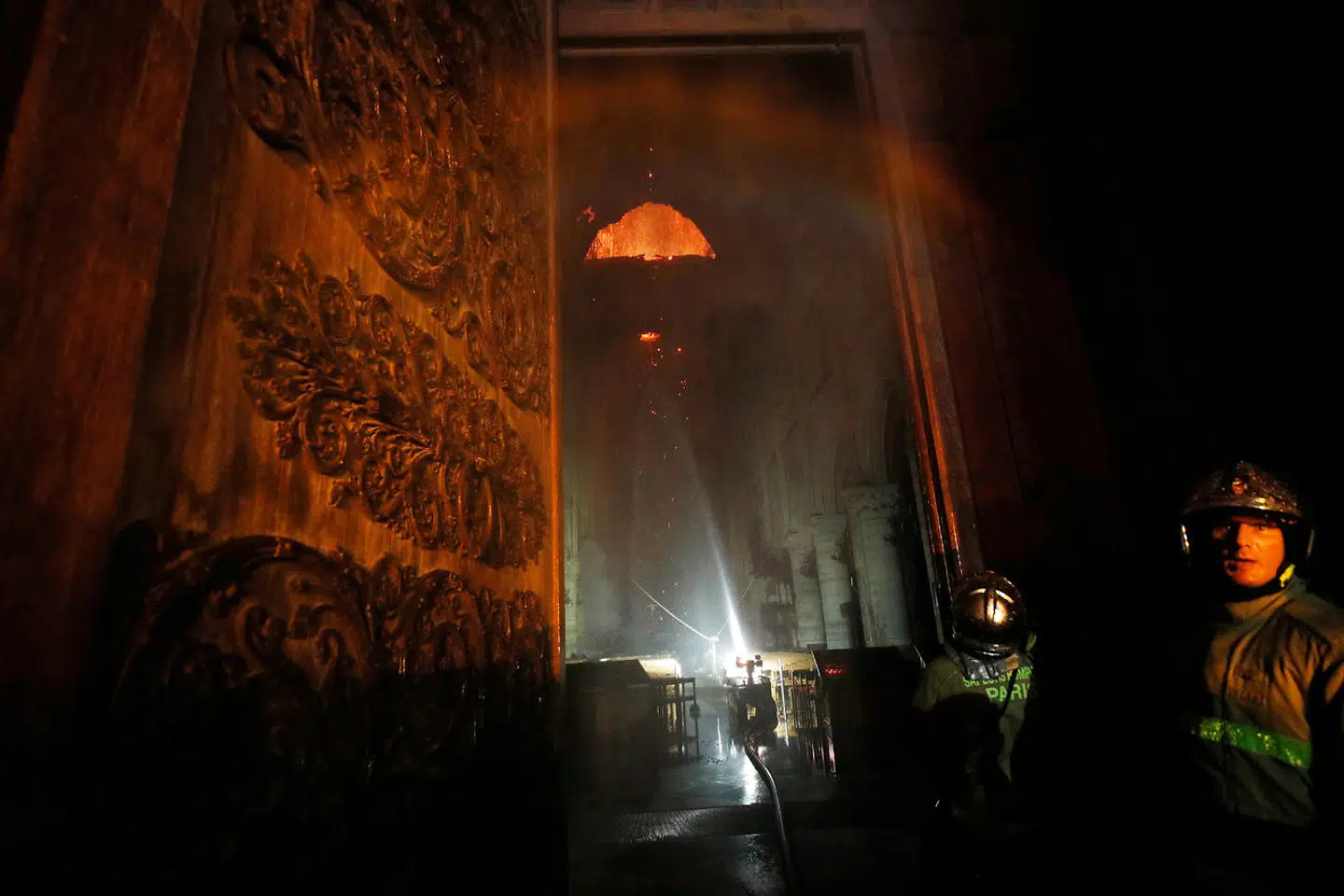 Paris Fire brigade members are seen at an entrance that looks into the Notre Dame Cathedral as a fire continues to burn in Paris, France, April 15, 2019. REUTERS/Philippe Wojazer