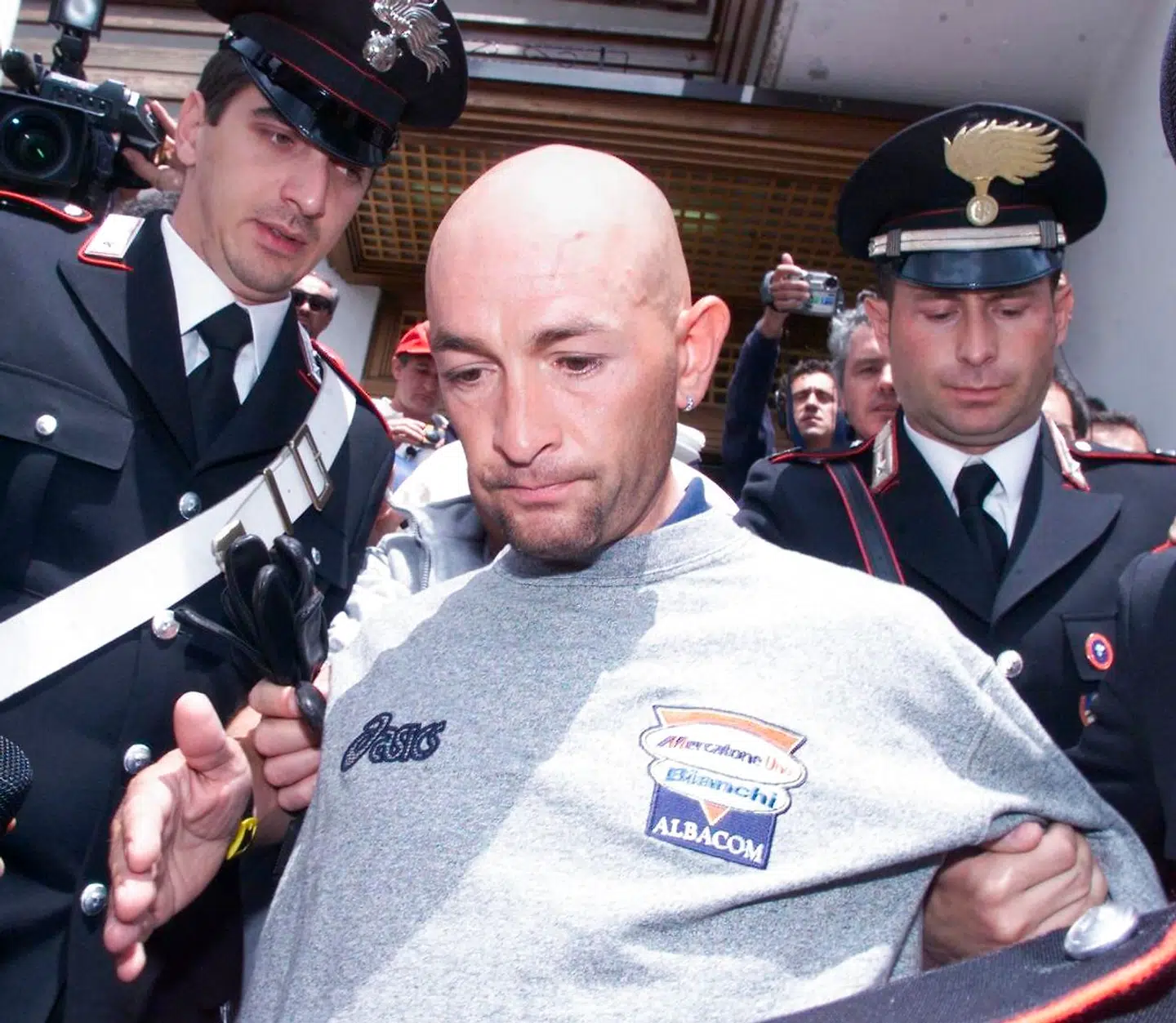 Marco Pantani bliver i 1999 eskorteret ud af sit hotel af italiensk politi, da han ikke bestod en blodtest og blev smidt ud af løbet.