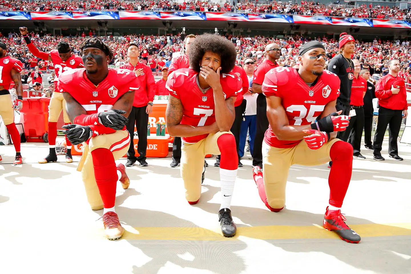 Colin Kaepernick (i midten) ses her knæe i oktober 2016 side om side med holdkammeraterne Eli Harold og Eric Reid.