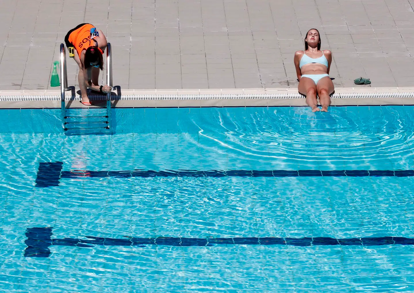 En ung kvinde solbader i sommervarmen med fødderne i et svalt svømmebassin. I den østspanske har hun nu ikke ret til at gøre det topløs. De kommunale myndigheder risikerer også bødestraf, hvis de ikke tillader bare bryster.