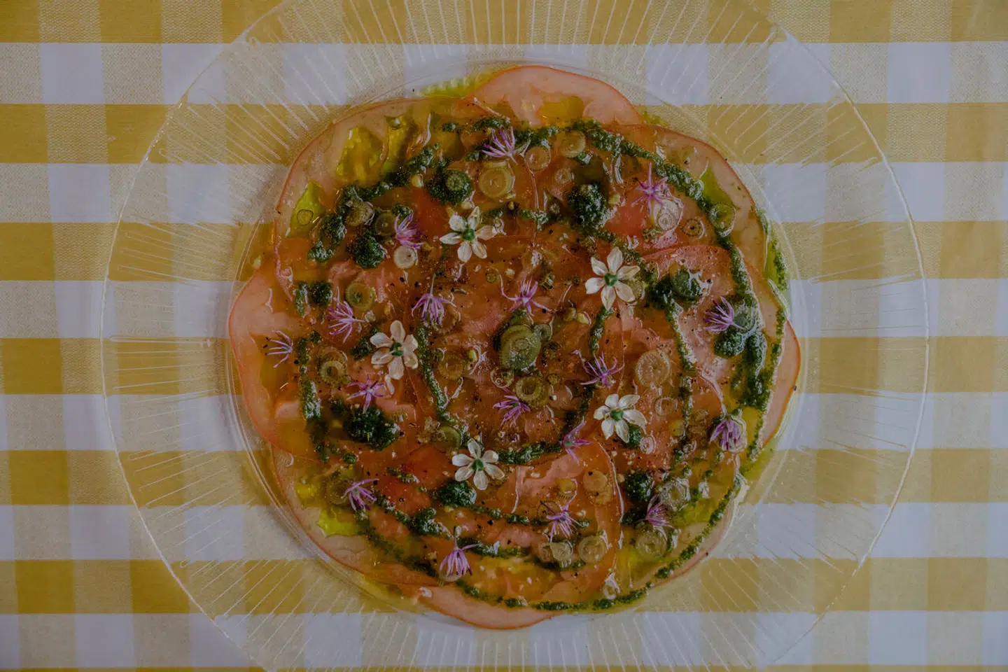 Tomatcarpaccio med med citron verbena-vinaigrette, syltede urtestilke og løgblomster.
