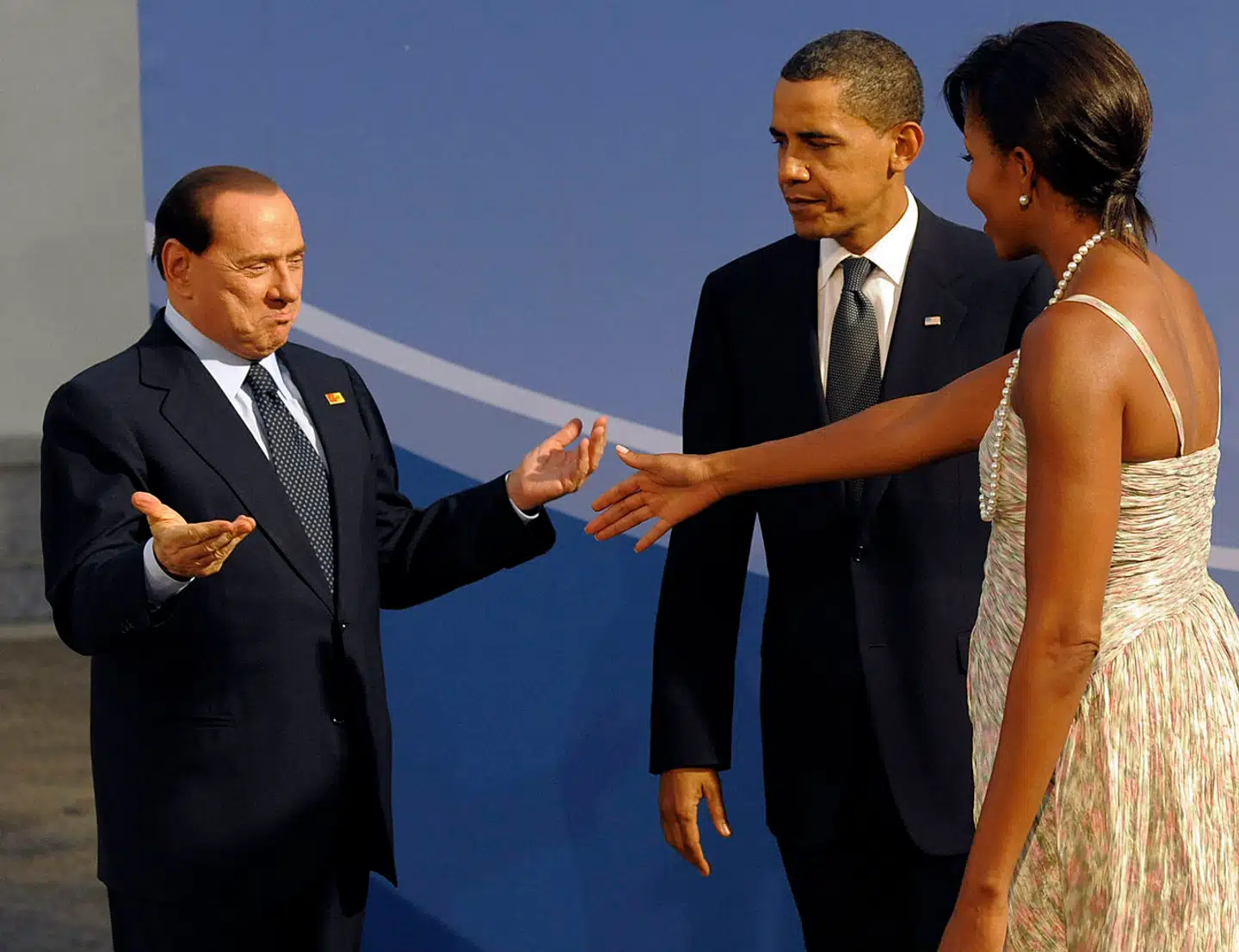 Silvio Berlusconi hilser på USAs daværende førstedame Michelle Obama med en sigende gestus under et besøg i 2009, mens hendes mand ser mellemfornøjet til.
