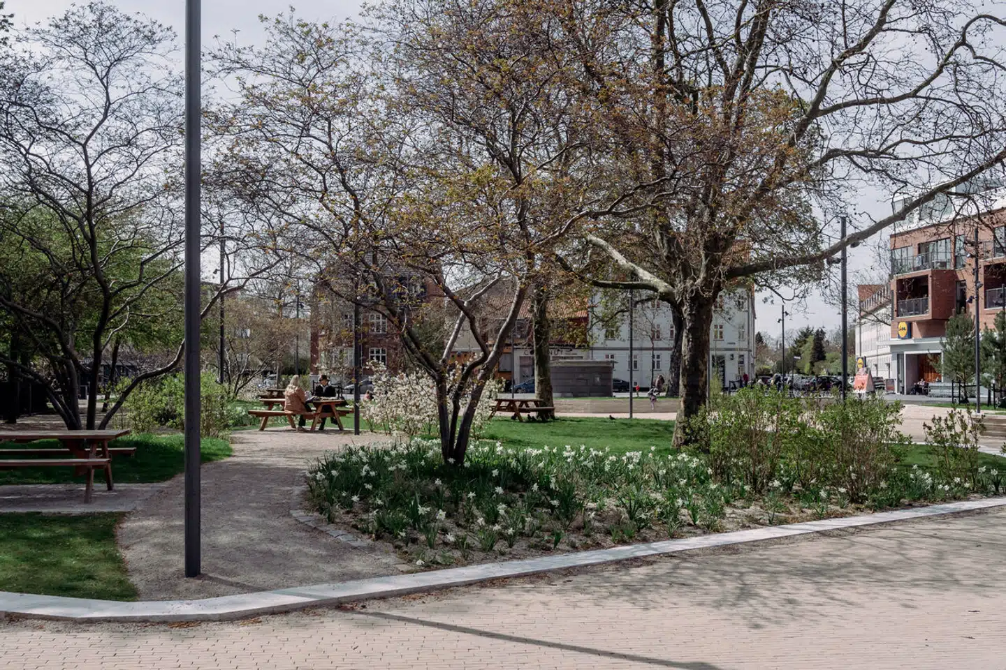 Pinseliljer og bærmispel står i blomst på Sundbyøster Plads. De meget profane bordogbænkesæt er med til at forankre den folkelige stemning.