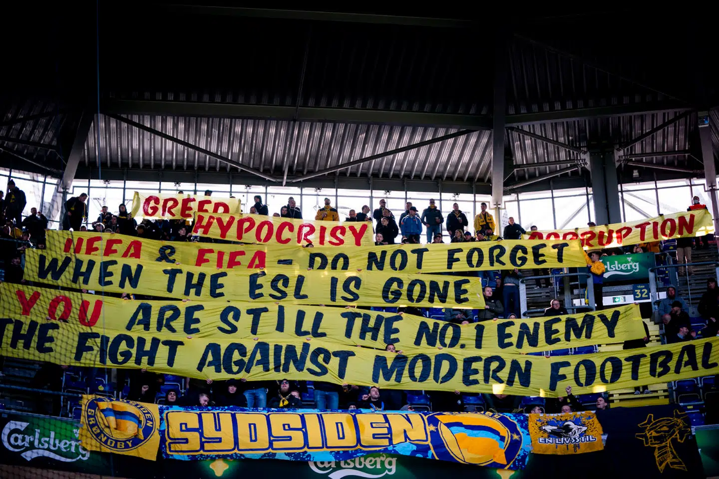 Global Football Holdings overtog i december aktiemajoriteten i Brøndby IF – siden har Fanafdelingen udtrykt stor kritik af, at Global Football Holdings ejer flere klubber, da det efter Fanafdelingens mening eliminerer klubbernes lokale særpræg. Billedet er fra superligakampen mellem Brøndby IF og Randers FC på Brøndby Stadion i april 2021, hvor fansene rettede skytset mod de internationale fodboldorganisationer UEFA og FIFA.