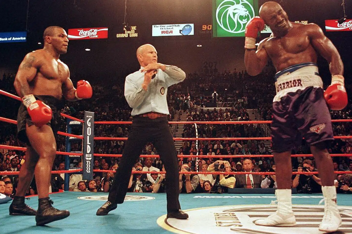 Kamplederen Lane Mills blev nødt til at stille sig ind i midten af ringen og stoppe boksekampen mellem Mike Tyson (til venstre) og Evander Holyfield. Holyfield tog sig til øret, fordi Tyson lige havde bidt en luns af det. Tyson blev kort efter diskvalificeret. Kampen blev bokset i MGM Grand Garden Arena i Las Vegas 28. juni 1997. Epa/Ritzau Scanpix