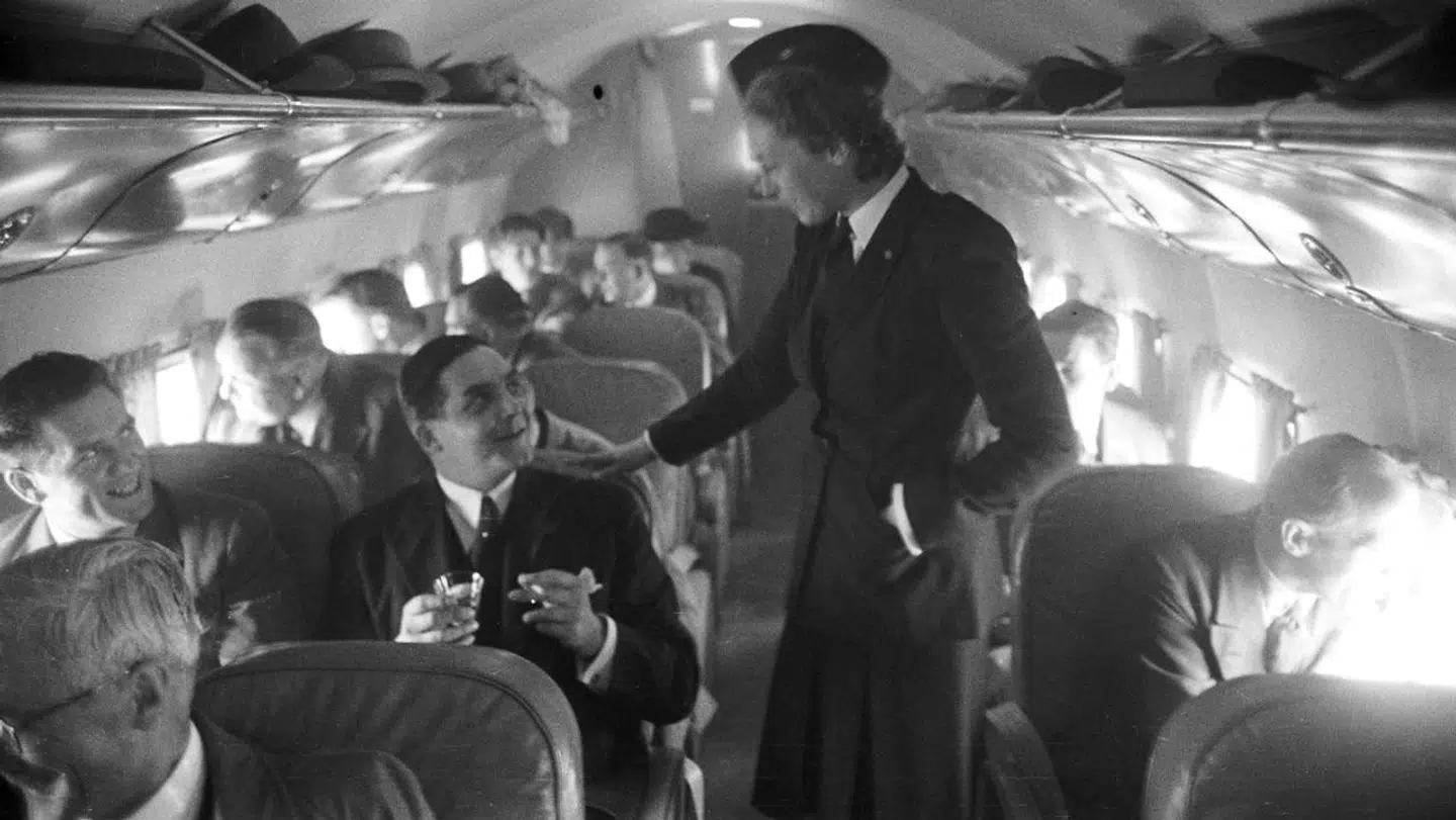 Et vue indenfor i et Douglas DC-3-fly fra det i 1946 nystartede, skandinaviske flyselskab SAS. En stewardesse taler med en af de rejsende, der sidder og ryger en cigaret.