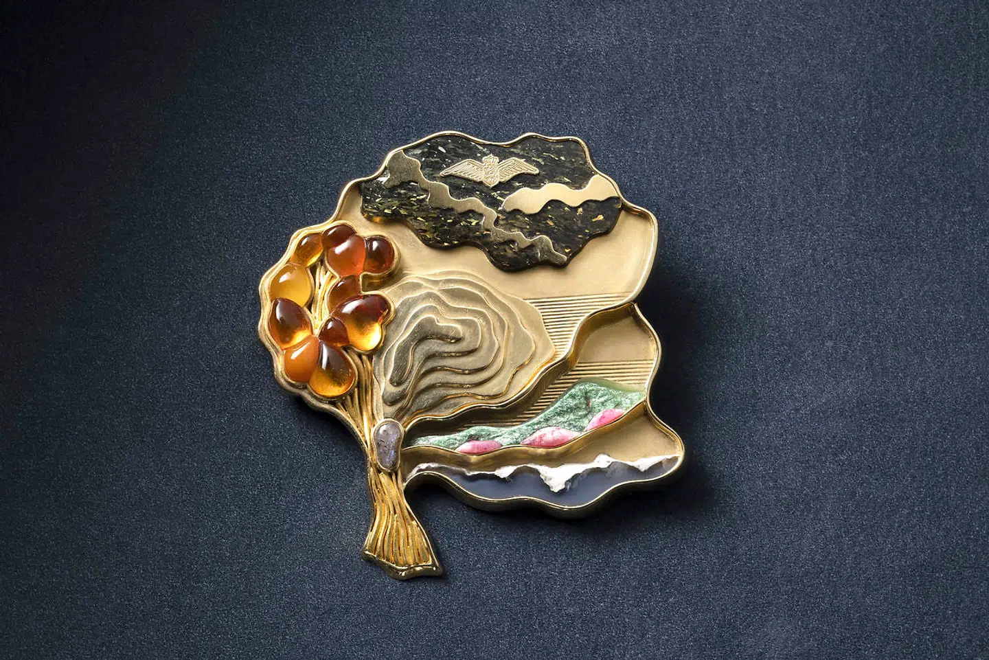 Guld med grønlandske stenarter og bornholmsk månesten. Udført i 1990 af Ole Kortzau. Gave fra Flyvevåbenets personel i 1990.