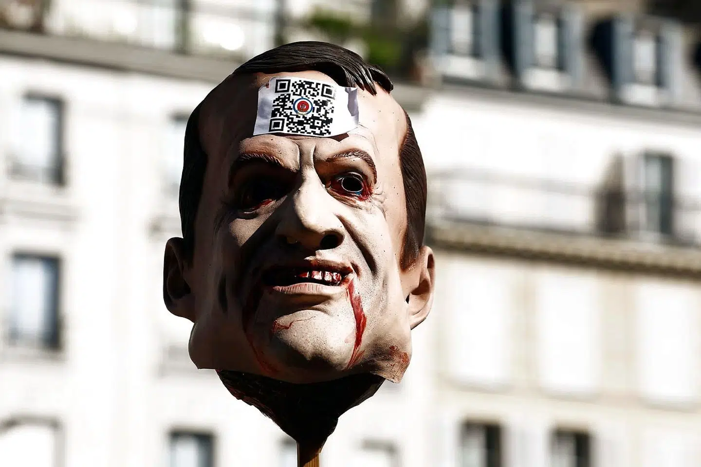 En maske, der forestiller Frankrigs præsident Emmanuel Macron, har fået klistret en af de blandt vaccinemodstandere forhadte QR-koder i panden under en protestdemonstration mod det allerede eksisterende coronapas.