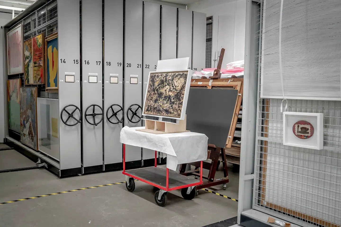 Jackson Pollock: »Black over Yellow«, 1950, på staffeli og på vej til eftersyn hos konservatorerne. Til højre for hænger Méret Oppenheims »Souvenir fra »Frokost i pels««, 1972, der læner sig op ad den berømte surrealistiske tekop i pels, som er udstillet på The Modern Museum of Art i New York.