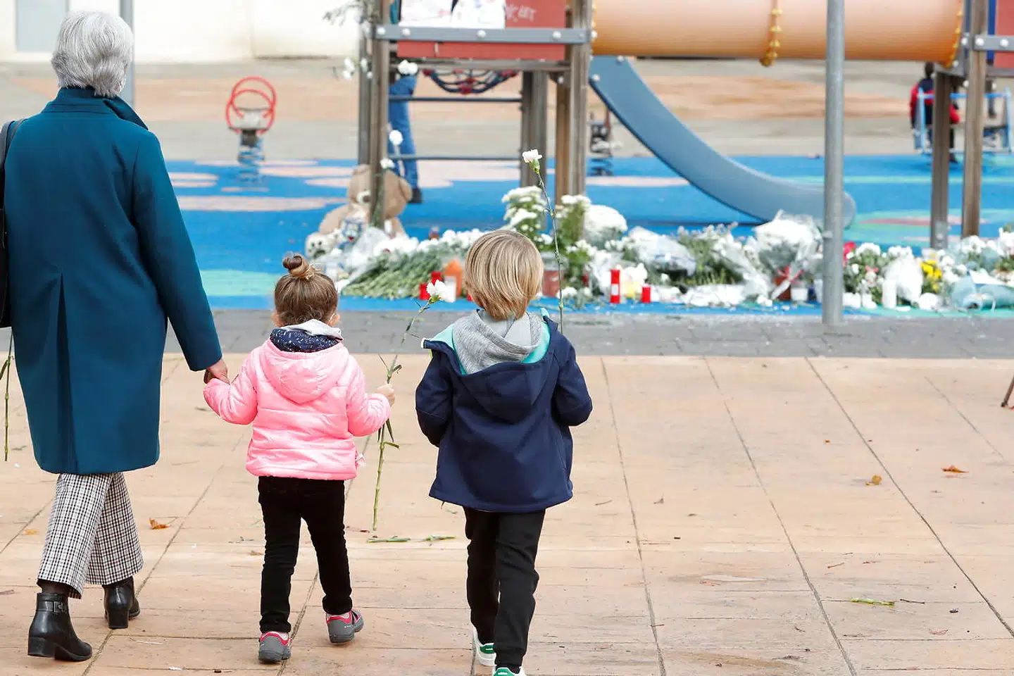 To børn og en ældre kvinde lægger blomster ved en mindelund på legepladsen i et nordspansk forstadskvarter, hvor niårige Álex torsdag blev lokket i døden af en mand, der allerede to gange er dømt for mord og seksuelle overfald.
