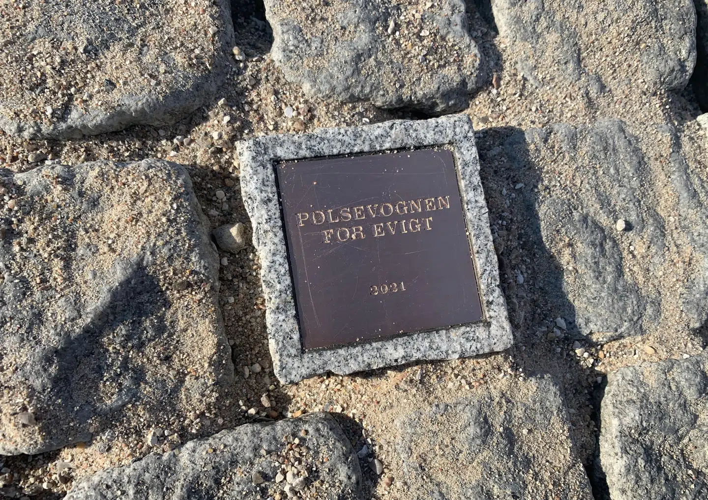 Danish Crown fik først på sommeren lov til at lægge en mindeplade ned på Rådhuspladsen. Den oprindelige så ud som på billedet, mens der i den endelige blev tilføjet: 'Opsat i forbindelse med pølsevognens 100-års jubilæum'.