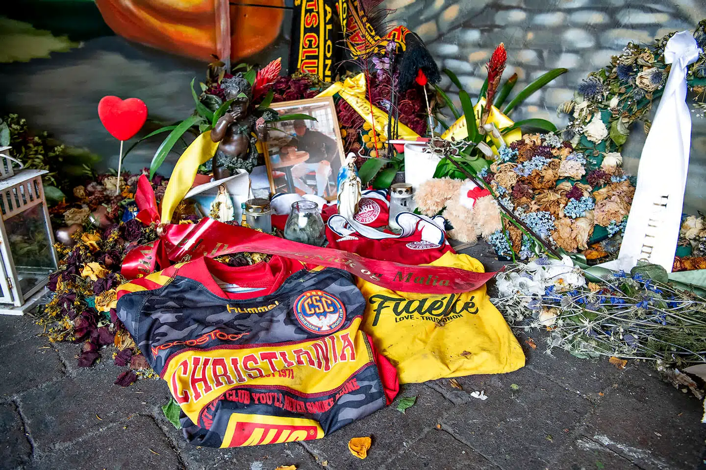 Ved siden af mindevæggen med den 22-åriges portræt ligger nogle af hans fodboldtrøjer, blomster og et billede. En christianit beskriver til Berlingske ham som »vennernes ven«. »Det var en meget fyldt Frelser Kirke, lad mig sige det sådan,« siger vedkommende.