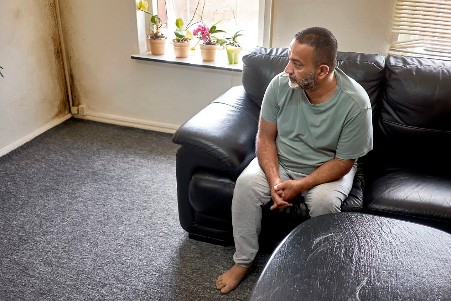 Khaled Alali sidder i sin stue i ejendommen i Faxe, hvor skimmelsvampen har bredt sig i hjørnet. Svampen er groet videre og har spredt sig til alle lejlighedens rum.