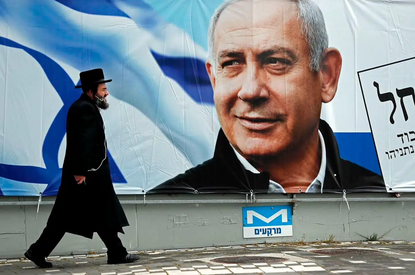 En ortodoks jøde går forbi en valgplakat med et portræt af Benjamin Netanyahu. Efter fire valg på to år er Netanyahu nu ikke længere premierminister. Israels nye regering bliver tvunget til moderation og kompromiser for at overleve, skriver Pierre Collignon i denne leder: »Det er en anden dynamik end den, som har drevet Benjamin Netanyahu.«