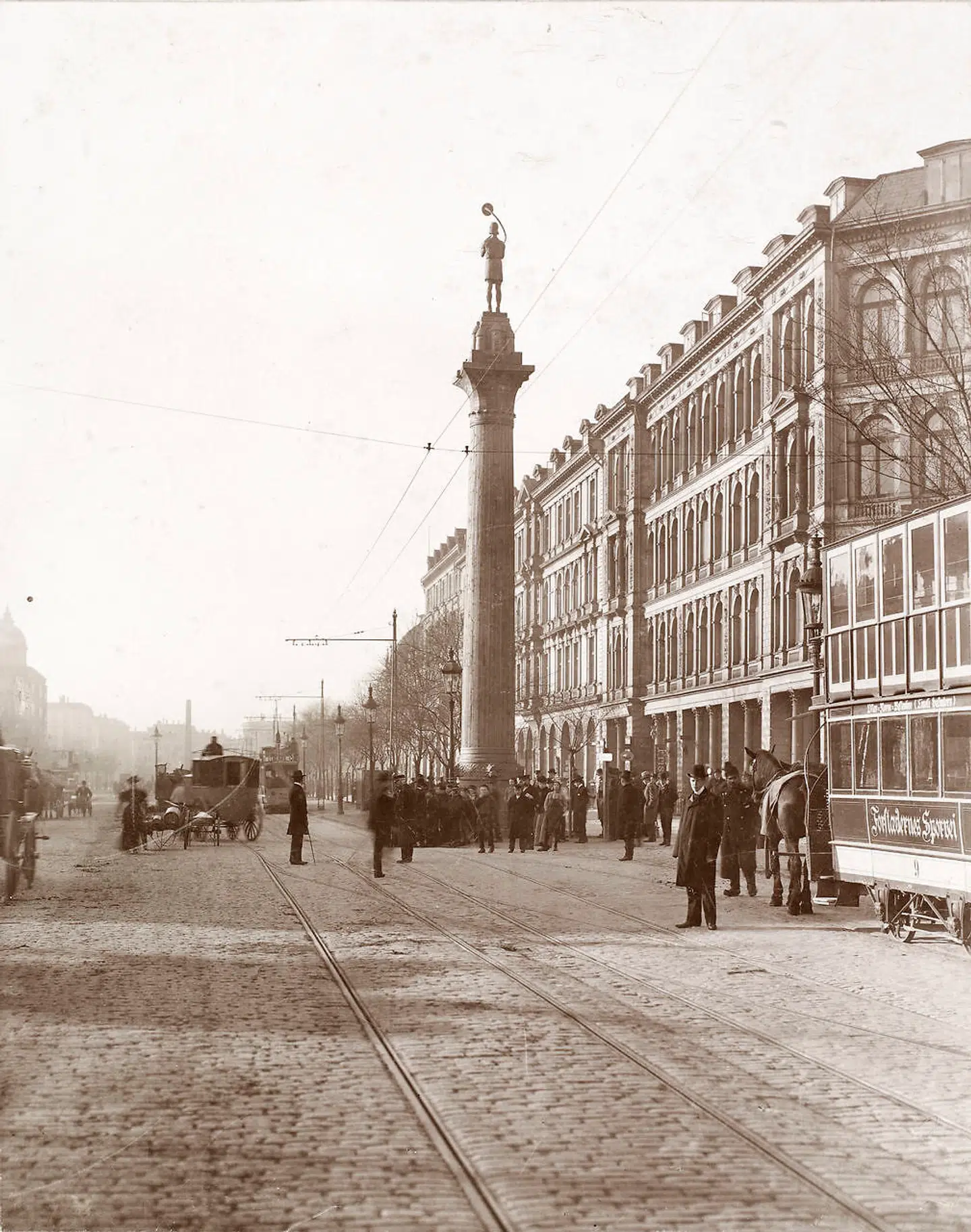 Prøveopstilling af lurblæseren foran Central Hotellet på Vesterbrogade i København, 1900. På en træsøjle er placeret en statue af en enkelt lurblæser udført af Anders Bundgaard. Julie Laurberg havde specialiseret sig i bl.a. arkitekturfotografering. Foto: Det Kgl. Bibliotek