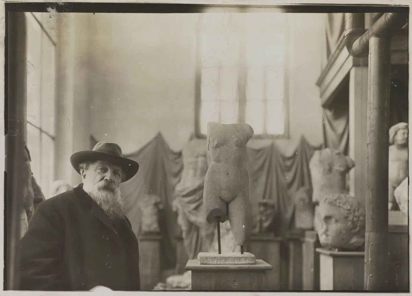 Rodin i sit atelier. Man ser både draperingerne og de fragmenterede antikviteter.