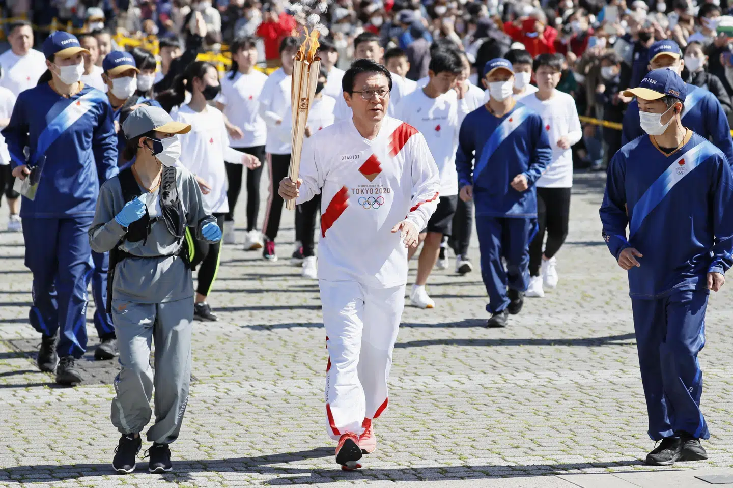OL-flammen er stødt på en udfordring i byen Osaka. Her ses flammen i hånden på den tidligere japanske OL-maratonløber Toshihiko Seko i byen Yokkaichi onsdag. Som det kan ses i baggrunden medfører det et væld af mennesker, og det vil man gerne undgå i Osaka. Unknown/Ritzau Scanpix