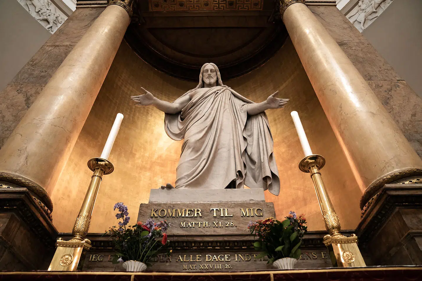 »Kirken har masser af koncerter, foredrag, højskolevirksomhed, samtalegrupper, udflugter og korsang – og så er der al kunsten lige fra billeder, altertavler og prædikestole til vinduesmosaik«. Vor Frue Kirke, Kristusstatue af Bertel Thorvaldsen.