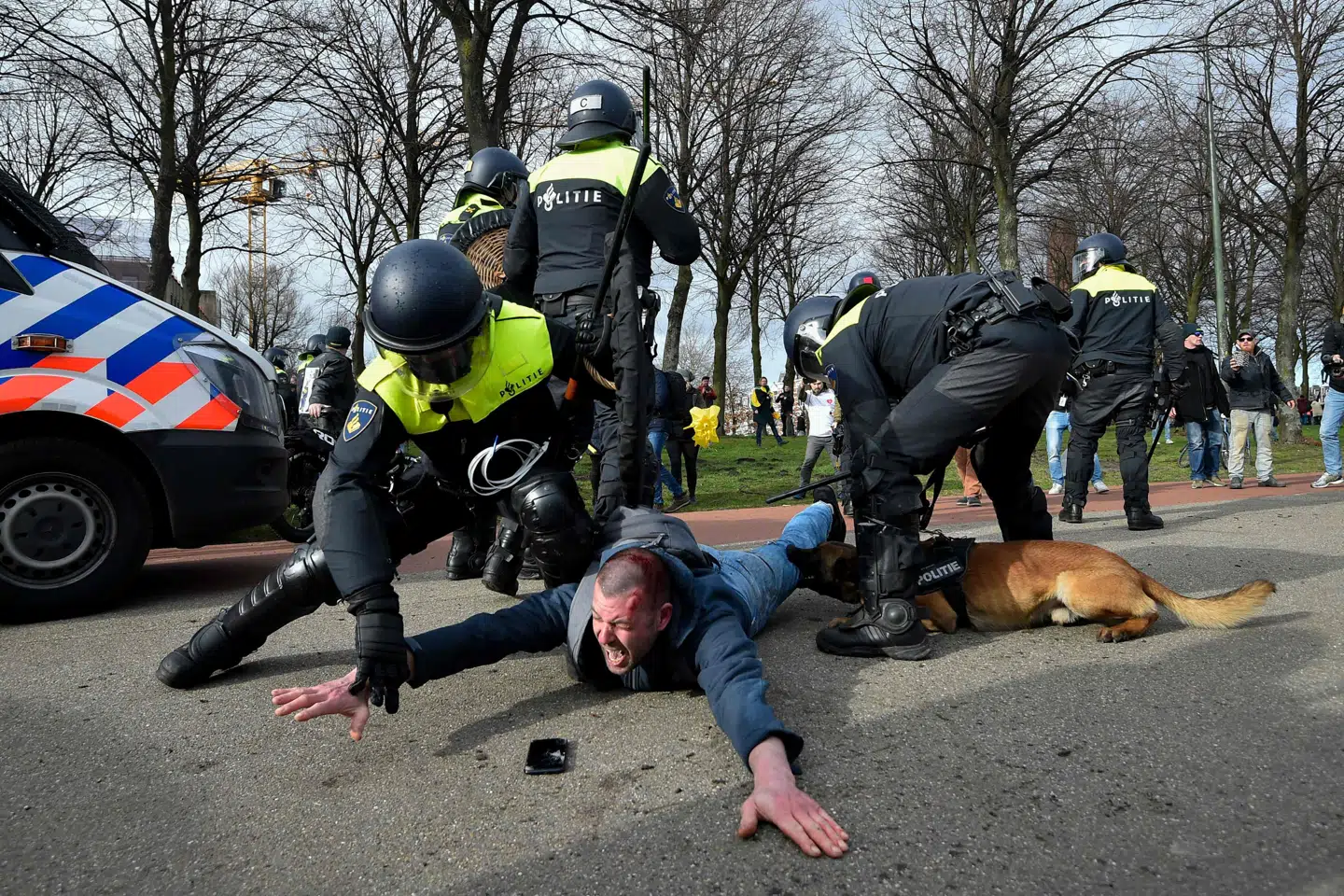 Kampklædt politi anholder en mand under en demonstration mod Hollands regering og coronanedlukningerne søndag i Haag. To demonstranter er blevet bidt af politihunde, og 20 er anholdt. John Thys/Ritzau Scanpix