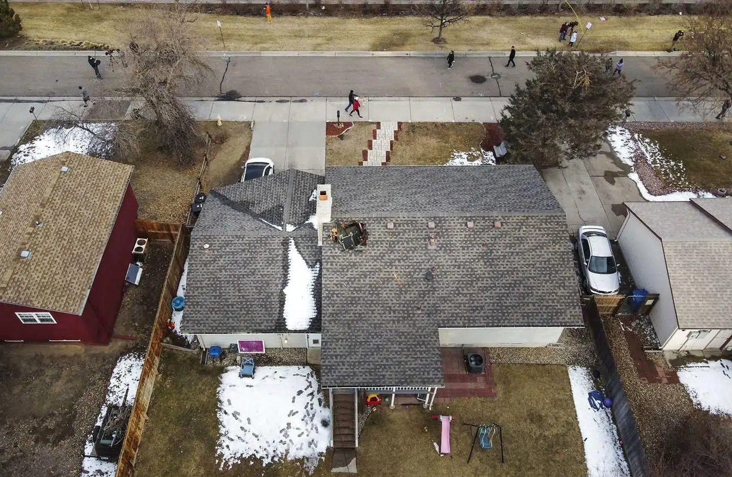 På et luftfoto ses folk gå forbi et hus i Broomfield, som nu har hul i taget, fordi vragdele fra Boeing 777-flyet ramte, efter at den ene motor eksploderede.
