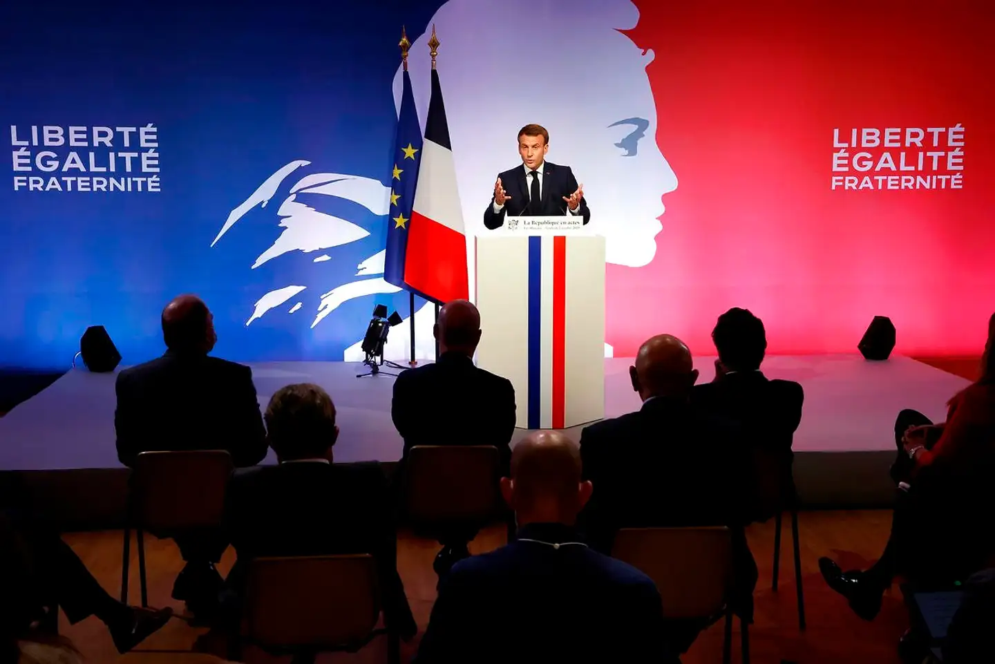 Scenografien var, som altid når det hander om Emmanuel Macron, formfuldendt, da den franske præsident præsenterede sin plan foran et billede af Republikkens symbolske figur, Marianne, og flankeret af det velkendte motto: frihed, lighed og broderskab.