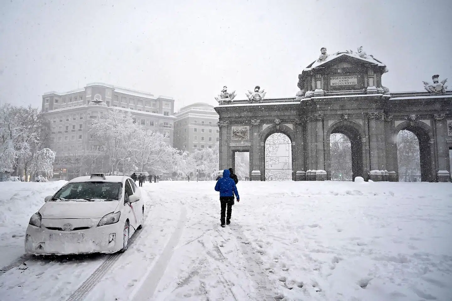 People walk past the Puerta de Alcala amid a heavy snowfall in Madrid on January 9, 2021. - Heavy snow fell across much of Spain, leaving huge areas blanketed in white as Storm Filomena brought wintry weather not seen in decades to the Iberian peninsula. (Photo by GABRIEL BOUYS / AFP)