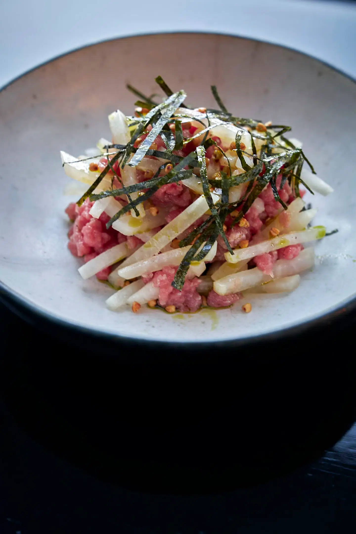 Tatar på oksekød med glaskål kogt i dashi-fond, toppet af noritang og ristede boghvedekerner.