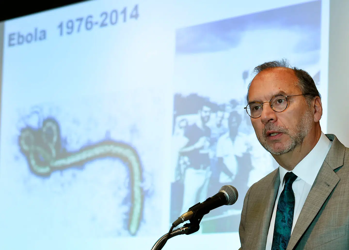 Læg mærke til planchen bag Professor Peter Piot på billedet. Den viser det ormelignende udseende på ebolavirussen, som forskere opdagede i 1976, da de fik inficeret blod under mikroskop.