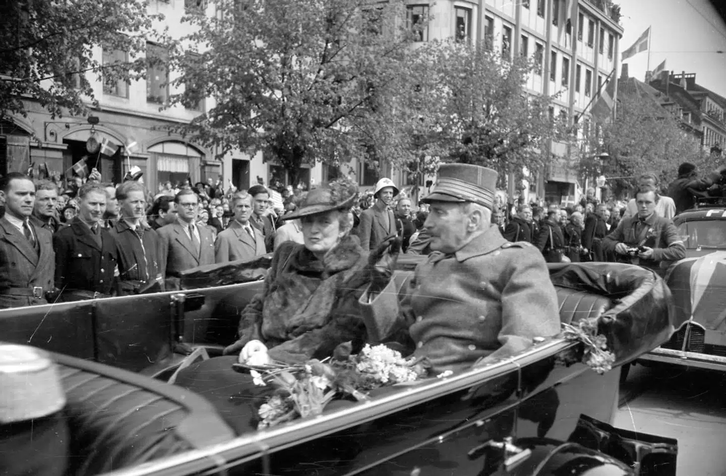 Kong Christian X og dronning Alexandrine kører i åben vogn gennem København i forbindelse med befrielsen 5. maj 1945. Langs vejen står folk med dannebrogsflag.