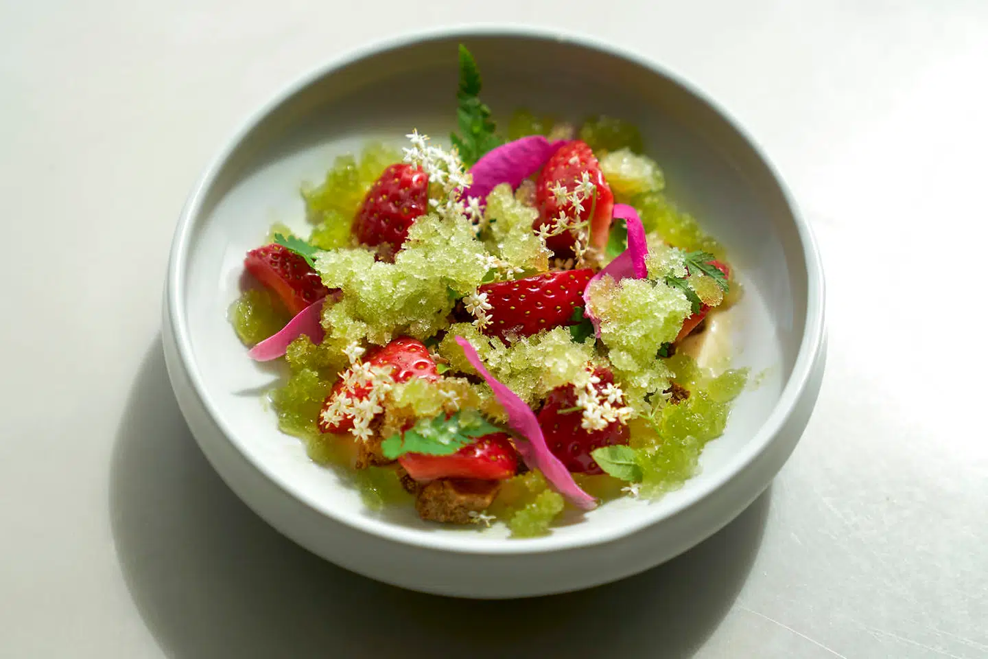 Panna cotta på vanilje, toppet af store stykker af brændt hvid chokolade, råsyltede jordbær, grøn granité på stikkelsbær og citronverbena samt rosa hybenroseblade.