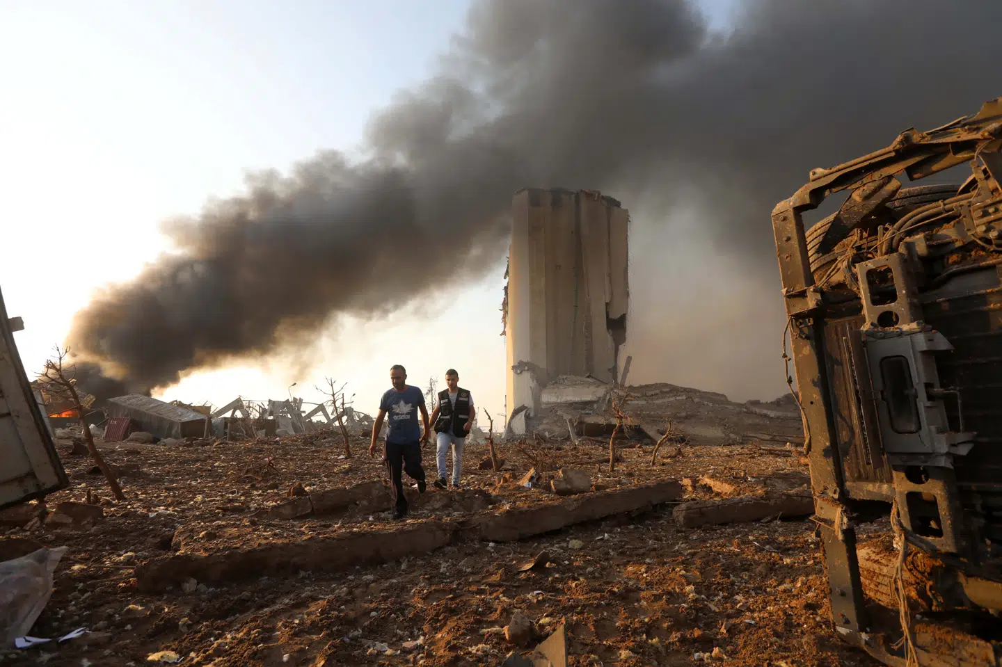 To mænd går rundt i det ødelagte havneområdet i Beirut. I kølvandet på eksplosionen er der stadig røg flere steder. Mohamed Azakir/Reuters