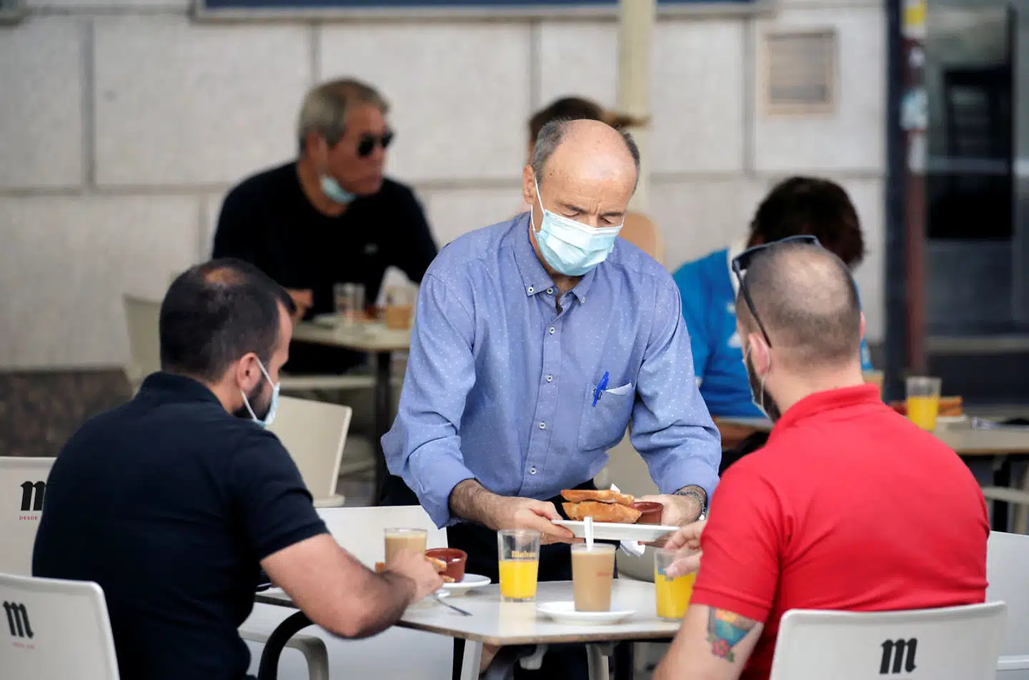 En tjener serverer café con leche, appelsinjuice og tostadas i Madrid. Da barerne åbnede igen efter forårets lange karantæne, skulle vi lige lære at håndtere beskyttelsesmaskerne som en obligatorisk rekvisit i coronapandemiens »nye normalitet«.