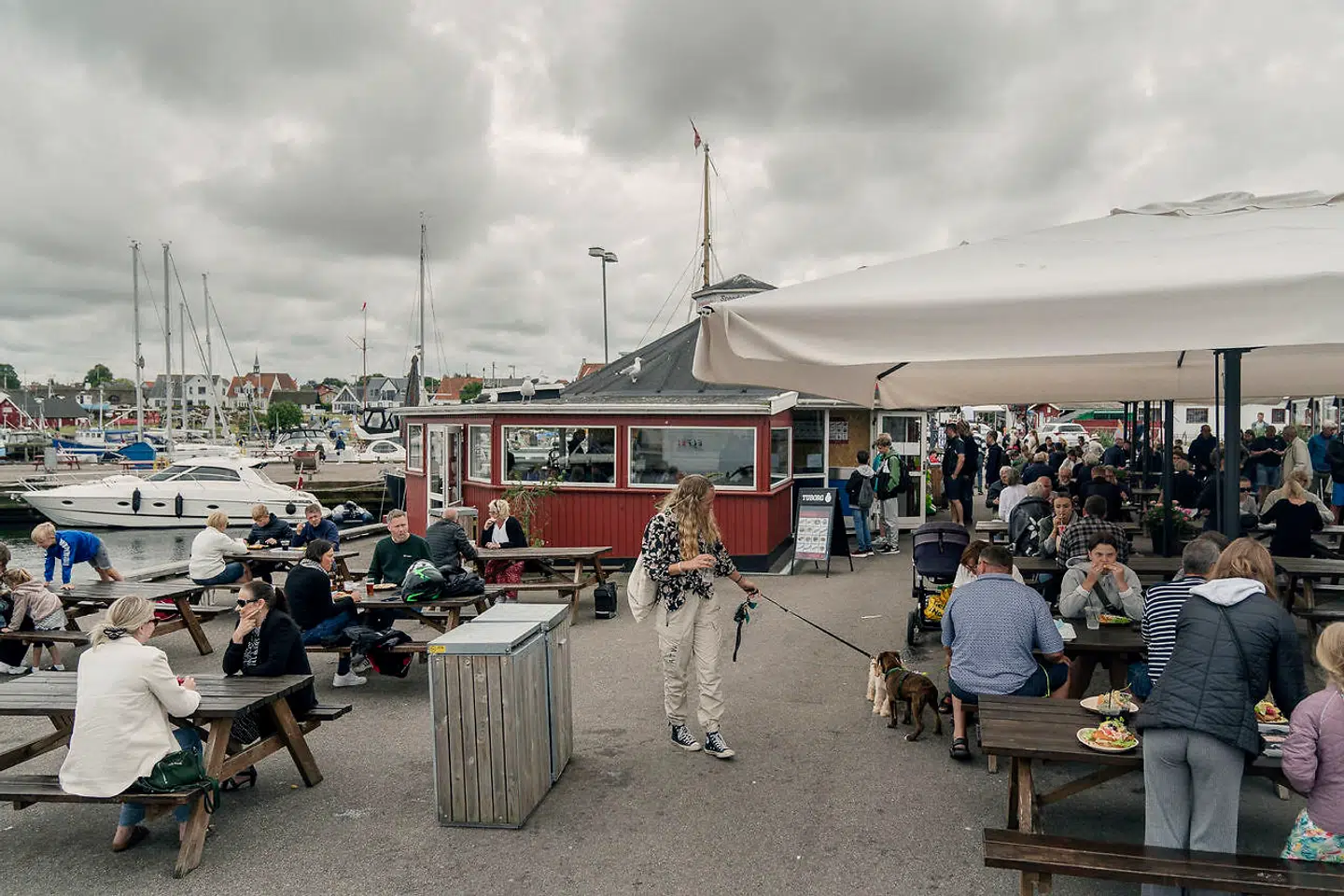 Der er godt gang i forretningen hos Adamsens Fisk ved Gilleleje. Mennesker flokkes rundt ved bordene for at spise fiskefilet, rejer og fiskefrikadeller.