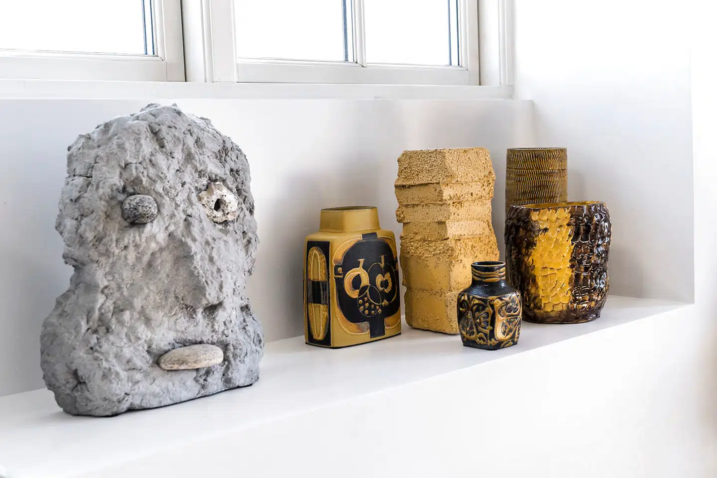Betonansigtet, som Uffe Buchardt kalder for Igor, og den gule høje betonvase i midten er af den dansk-norske duo Pettersen Hein. Den store brune og gule vase er af E. Michaelsen (1977). Vasen helt i baggrunden er vintage fra Tokyo, og de to små dekorerede vaser er Niels Thorsson for Royal Copenhagen.