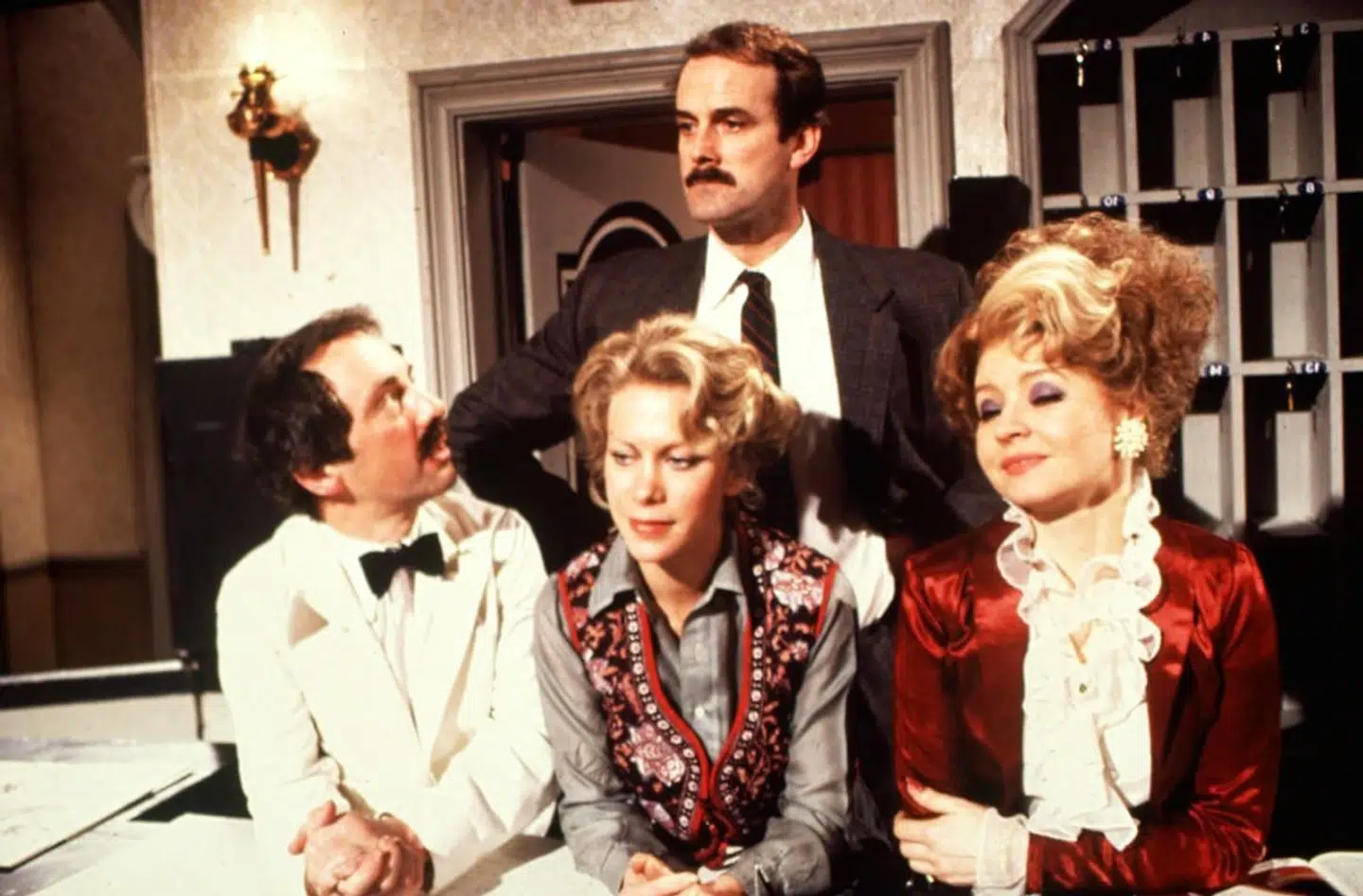Den engelske komiker John Cleese spiller hovedrollen i »Halløj på badehotellet«. Han har også skrevet serien sammen med sin daværende hustru, Connie Booth (i midten).