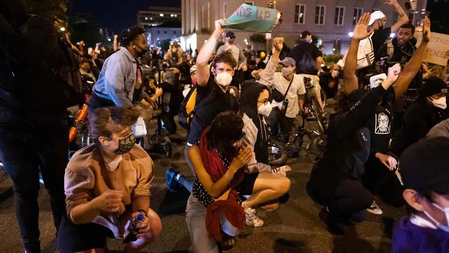 Demonstranter holder hænderne oppe for at forsøge at finde fodfæste i turbulensen skabt af en helikopter.