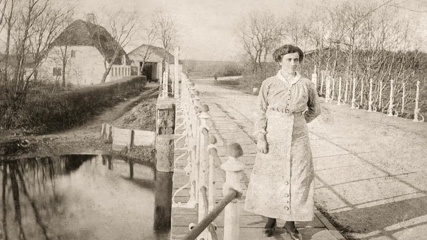 Karen Poulsen står ved Gelsbro i 1916. Hun var tjenestepige på kroen, der ses til venstre, og hun hjalp dansksindede desertører med at flygte over grænsen, så de undgik tysk militærtjeneste.