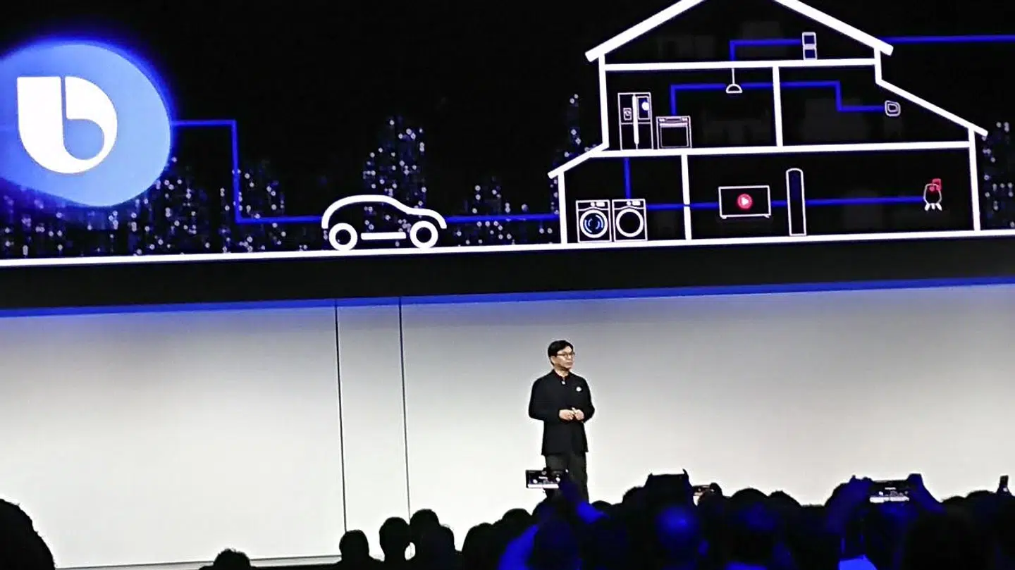 Samsung Electronics' topchef, H.S. Kim, forklarer her på en elektronikmesse, hvordan de digitale assistenter – her Samsungs egen Bixby i form af det blå logo til venstre – ved brug af kunstig intelligens kan sætte en kæde af hændelser sammen i og omkring det smarte hjem og styre for eksempel opvarmning af bilen, tænde og slukke lyset eller vaskemaskinen og finde film eller TV-programmer, som ligner dem, man sad og så i aftes.