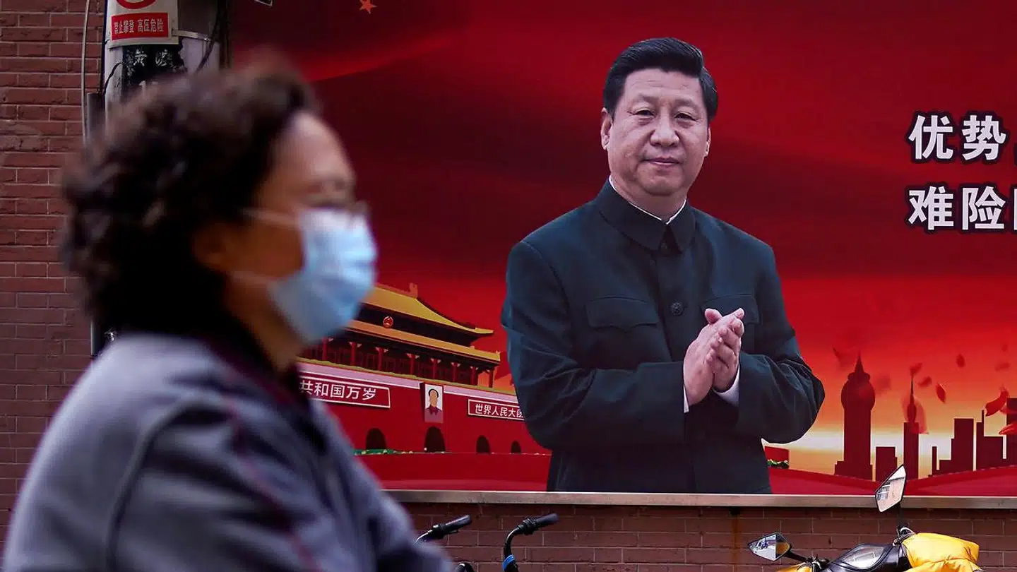 En kvinde med mundbind går forbi et portræt af Kinas præsident, Xi Jinping, 12. marts 2020.
