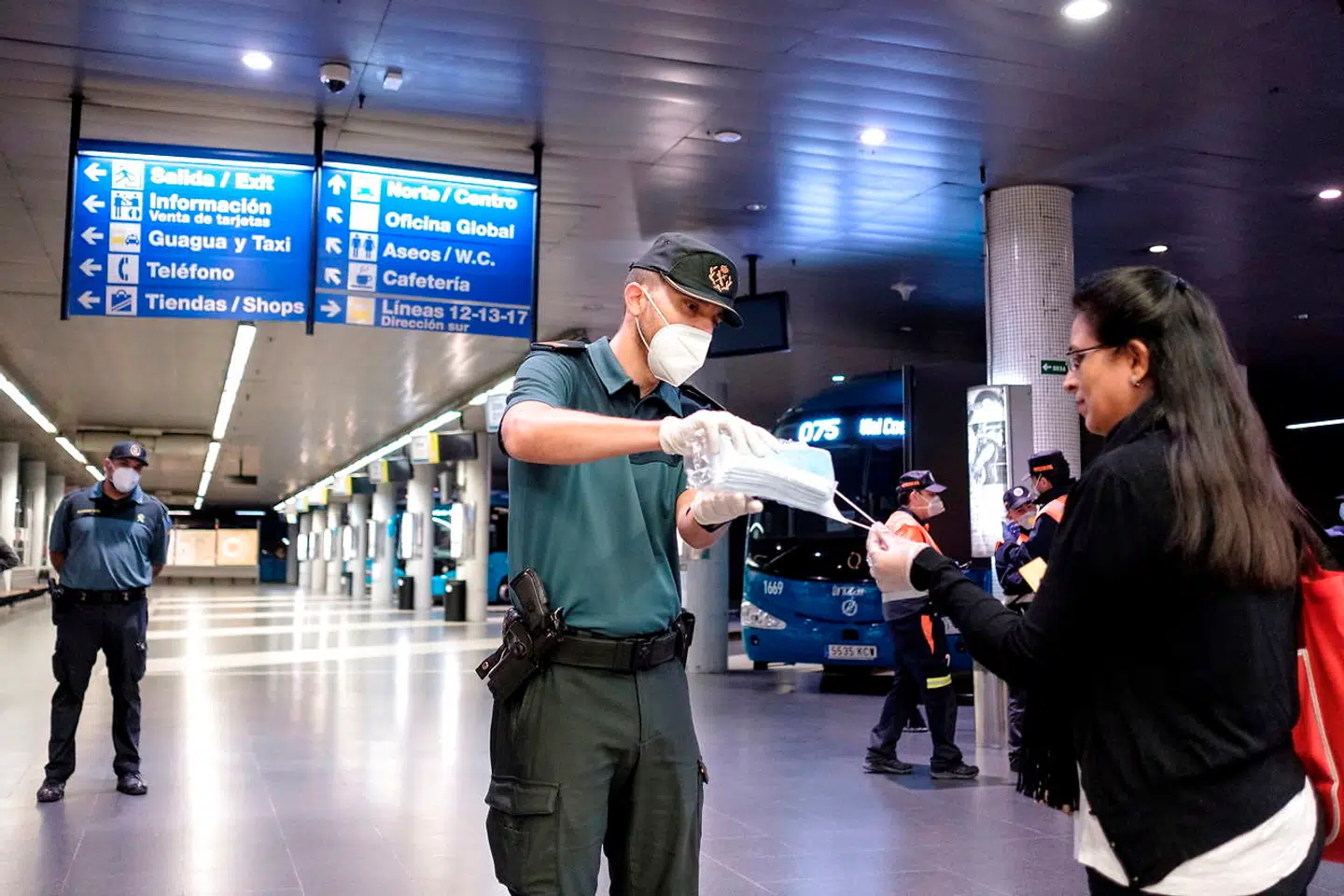 En civilgardist rækker et mundbind til en passager på busstationen i Gran Canarias hovedby, Las Palmas. De spanske myndigheder deler i alt ti millioner af dem ud i forbindelse med disse dages ophævelse af det totale lockdown.