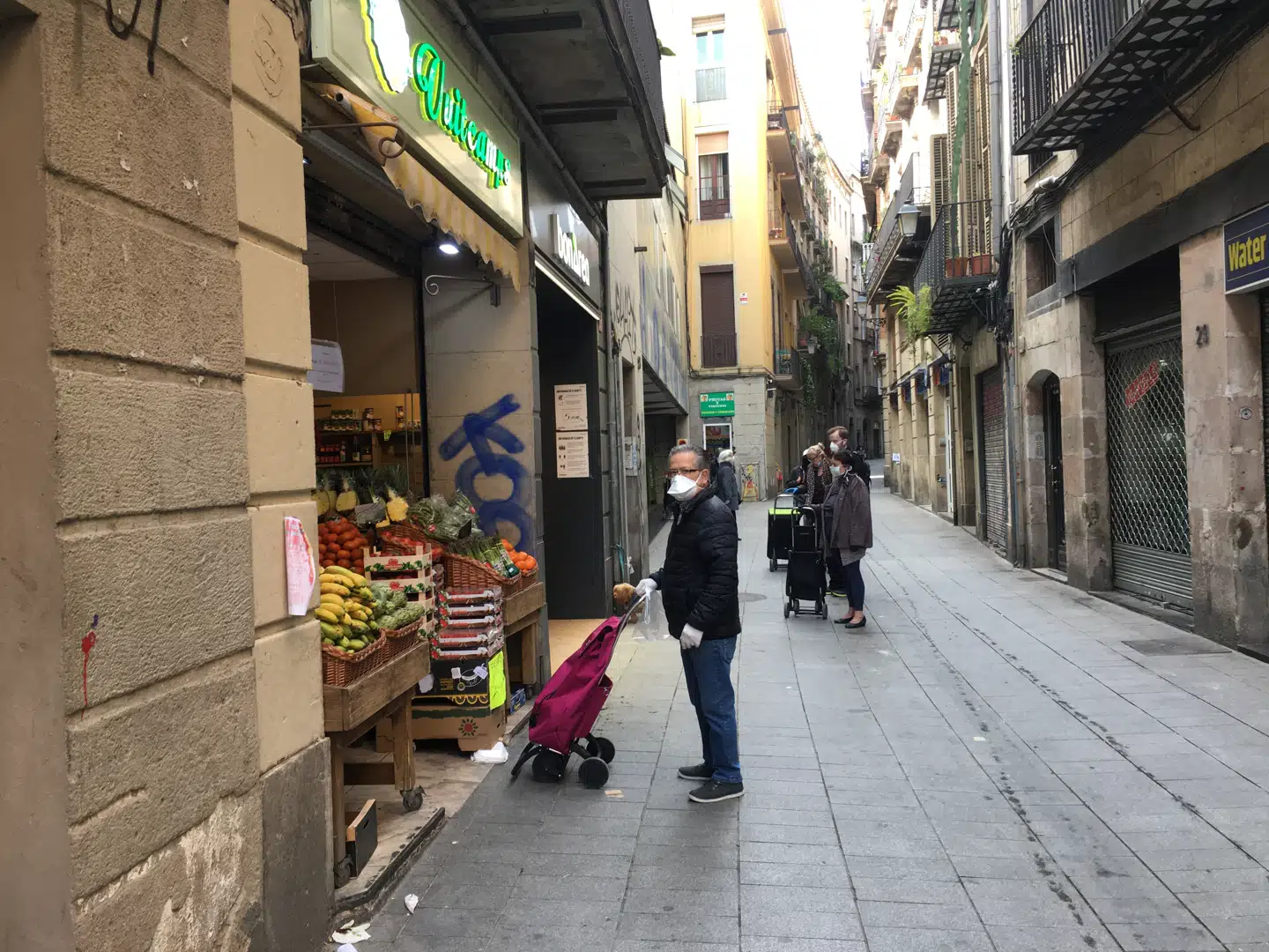 Kunder står i kø med forsvarlig sikkerhedsafstand uden for en grønthandler i det centrale Barcelona.