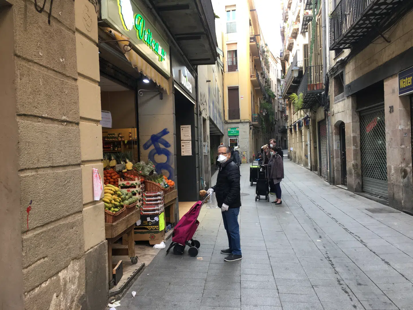 Kunder står i kø med forsvarlig sikkerhedsafstand uden for en grønthandler i det centrale Barcelona.