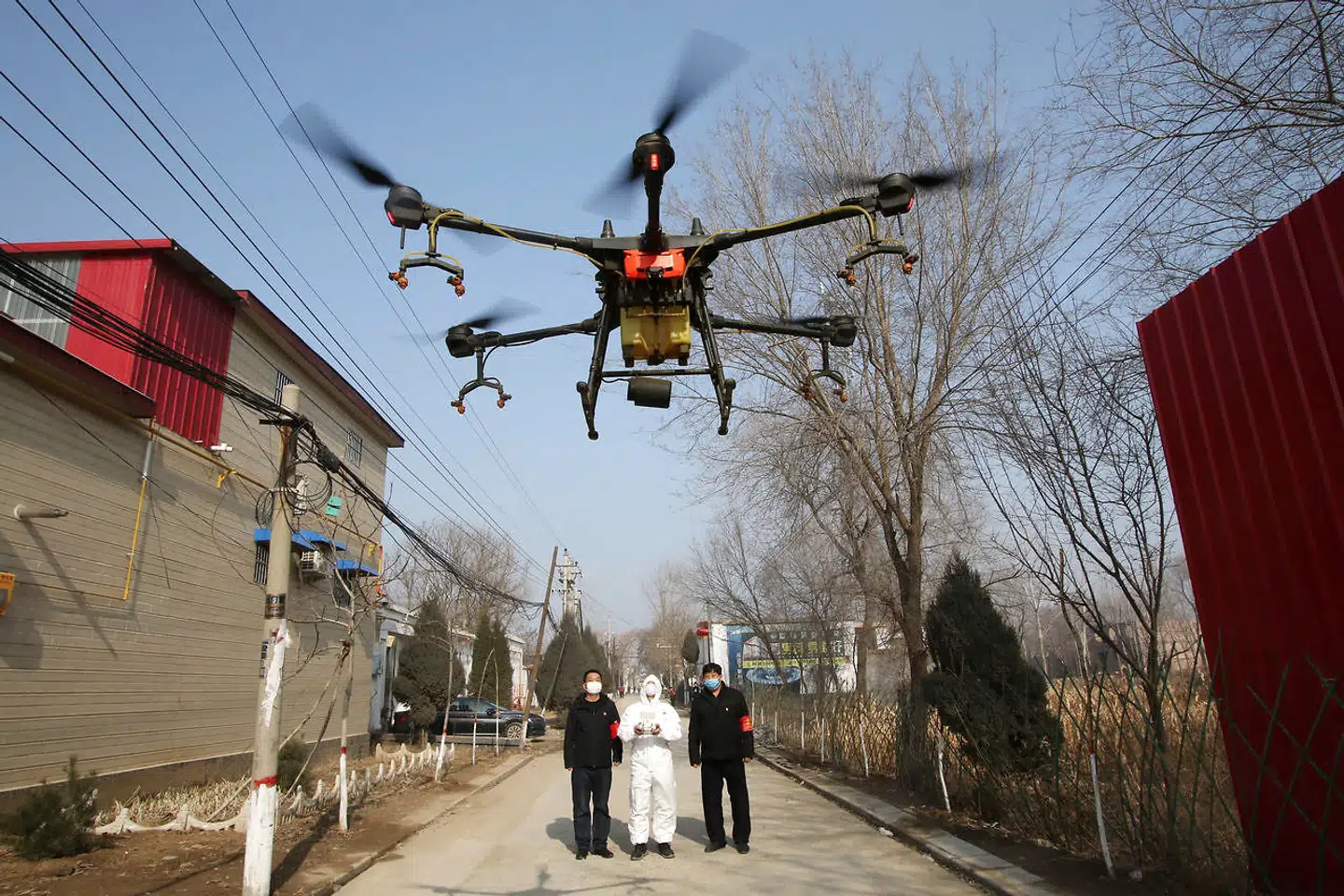 Frivillig i beskyttende dragt kontrollerer en drone, som sprayer desinfektionsmiddel i Zhengwan.