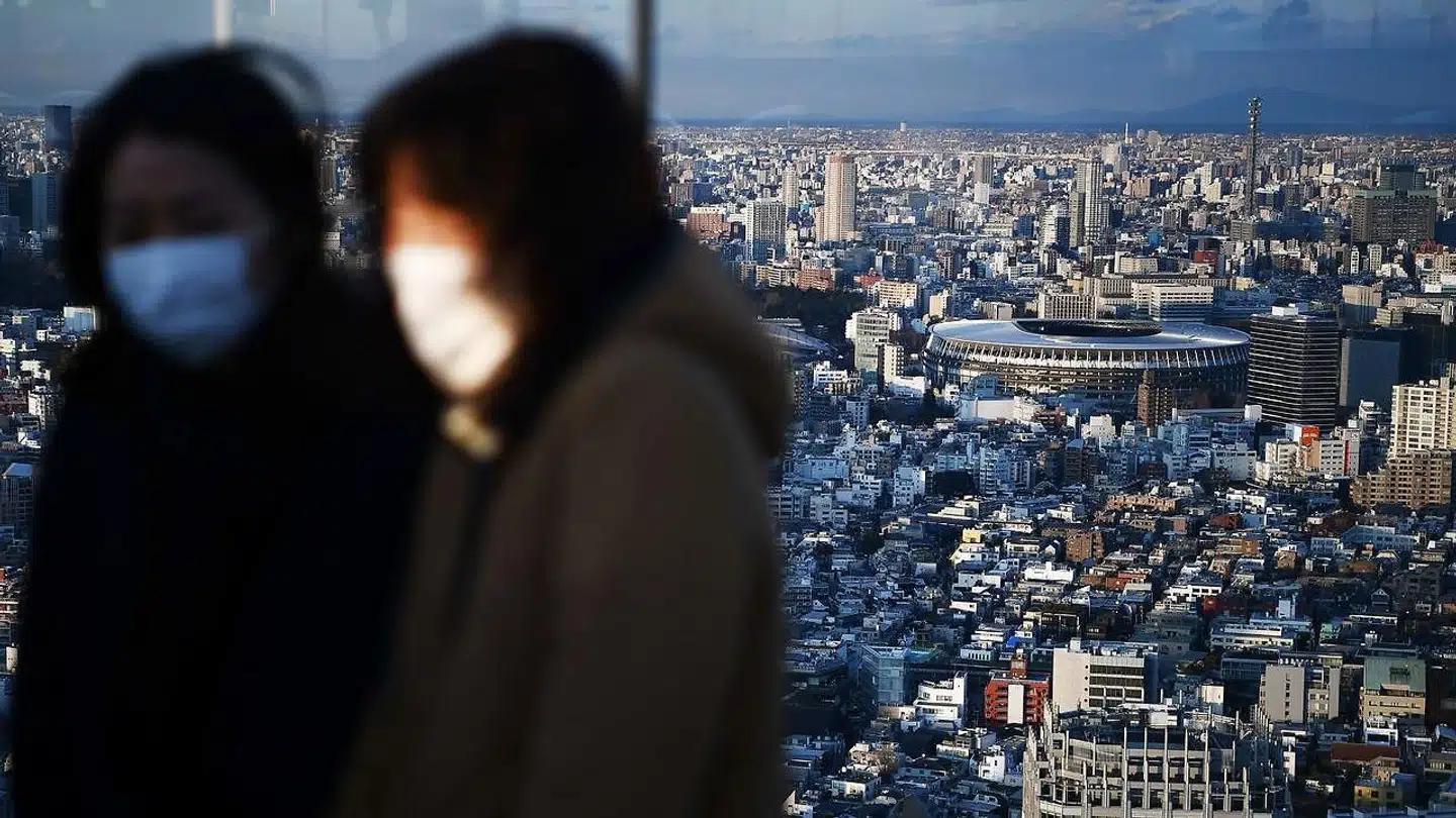 Turister med beskyttelsesmasker i toppen af en skyskraber i Tokyo med udsyn over megabyen og dens nybyggede OL-stadion. Den nye coronavirus risikerer at kaste mørke skygger over OL, der indledes om fem måneder.