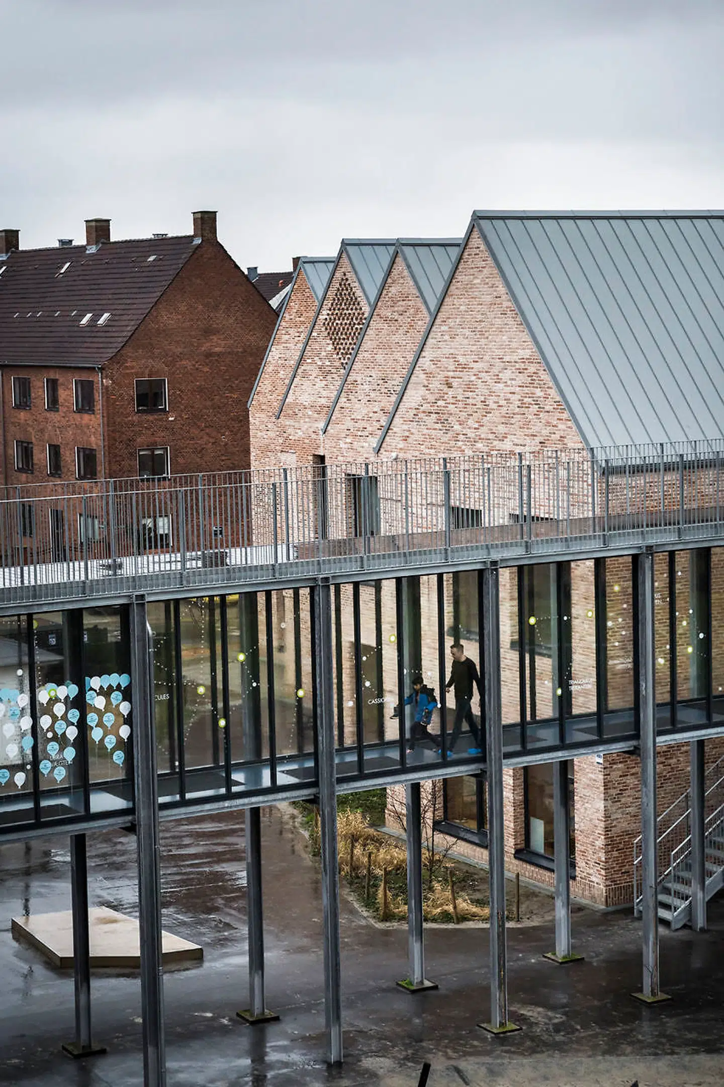 De falske længer passer meget fint ind i kvarterets øvrige arkitektur, men gangbroen mellem den gamle og de nye bygninger er alt for brutal.