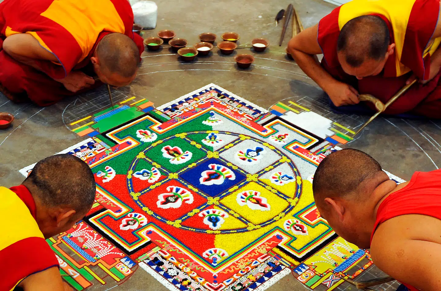 Tibetanske buddhistiske munke opbygger møjsommeligt en kompleks »mandala« med farvet sand.