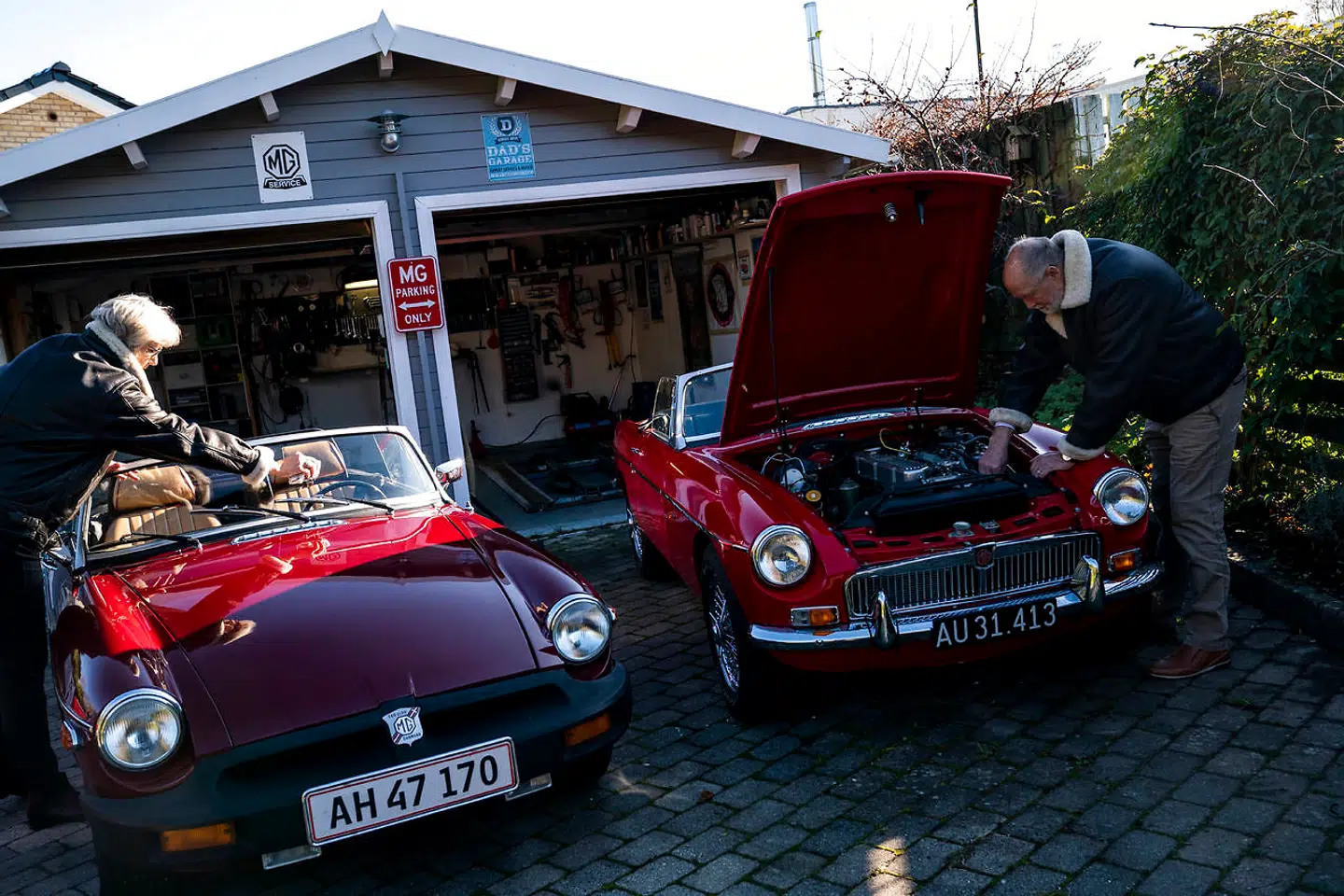 Linda pudser ruden på MGBen, mens Jens kigger til motoren i MGCen.